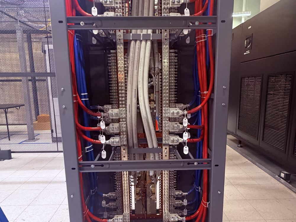 Rear view of a DC power distribution frame with red and blue feeders landed on compression lugs and copper busbar
