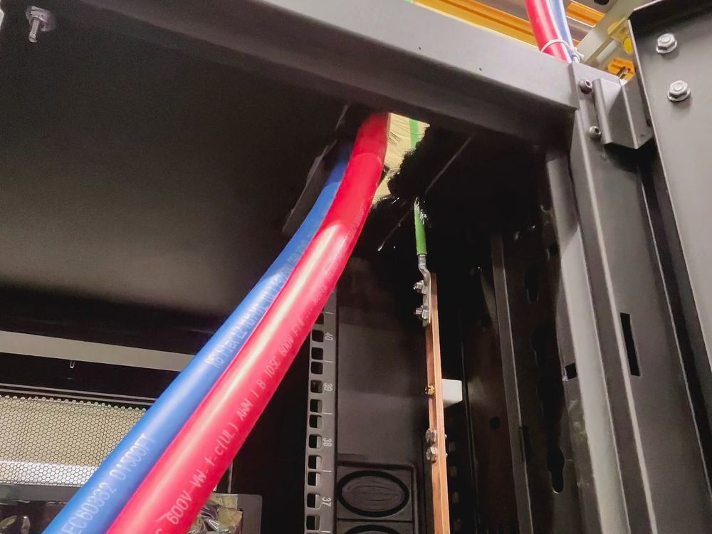 Close view of red and blue minus 48 volt feeders entering a cabinet alongside a copper ground bar