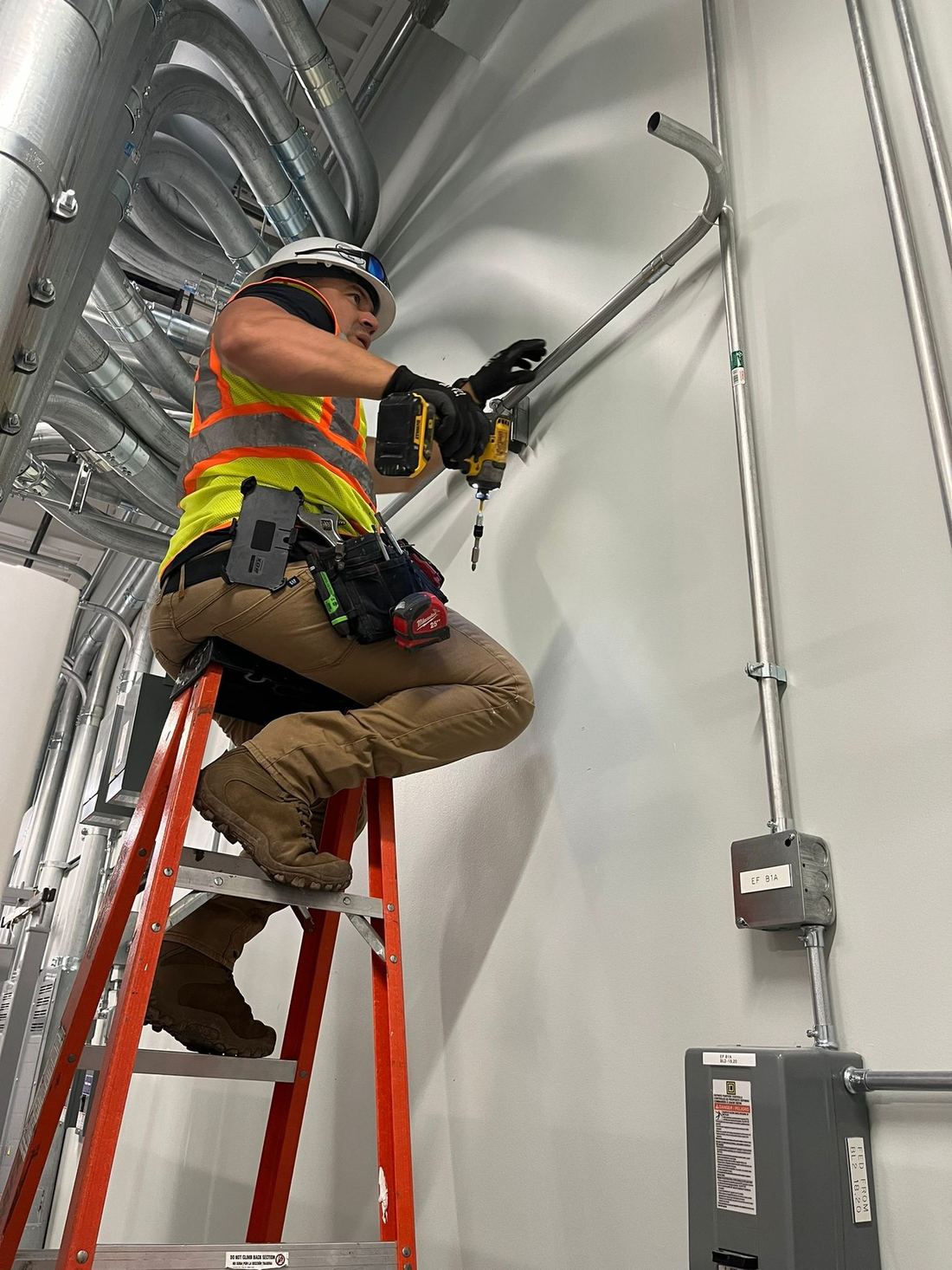 Technician installing EMT conduit and electrical feeder on wall